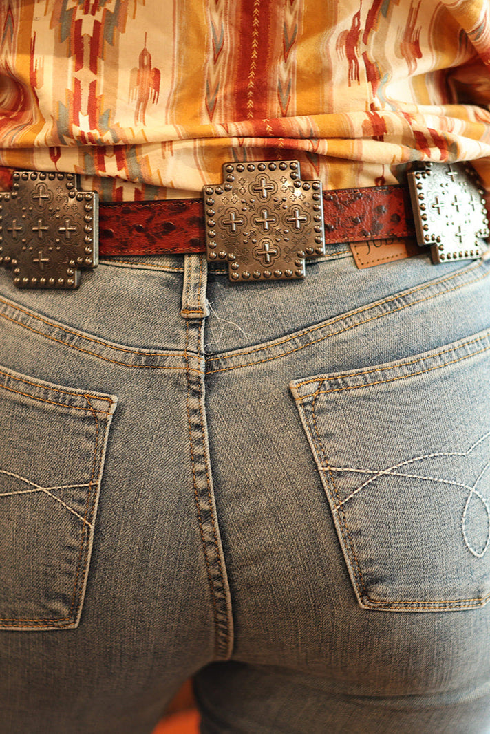 Person wearing a patterned shirt and jeans with a belt, standing indoors.