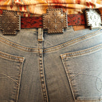 Person wearing a patterned shirt and jeans with a belt, standing indoors.