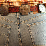 Person wearing a patterned shirt and jeans with a belt, standing indoors.