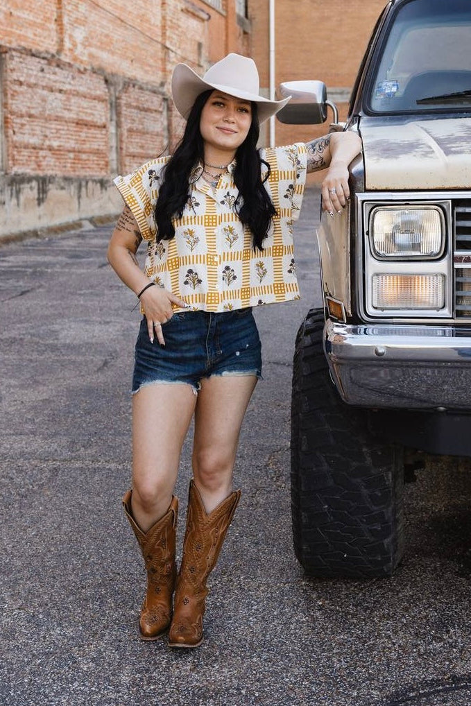 Woman in a checkered shirt and denim shorts standing next to a large truck.