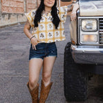 Woman in a checkered shirt and denim shorts standing next to a large truck.