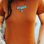 A person wearing a brown fitted t-shirt with a decorative necklace and a patterned skirt.