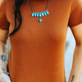 A person wearing a brown fitted t-shirt with a decorative necklace and a patterned skirt.