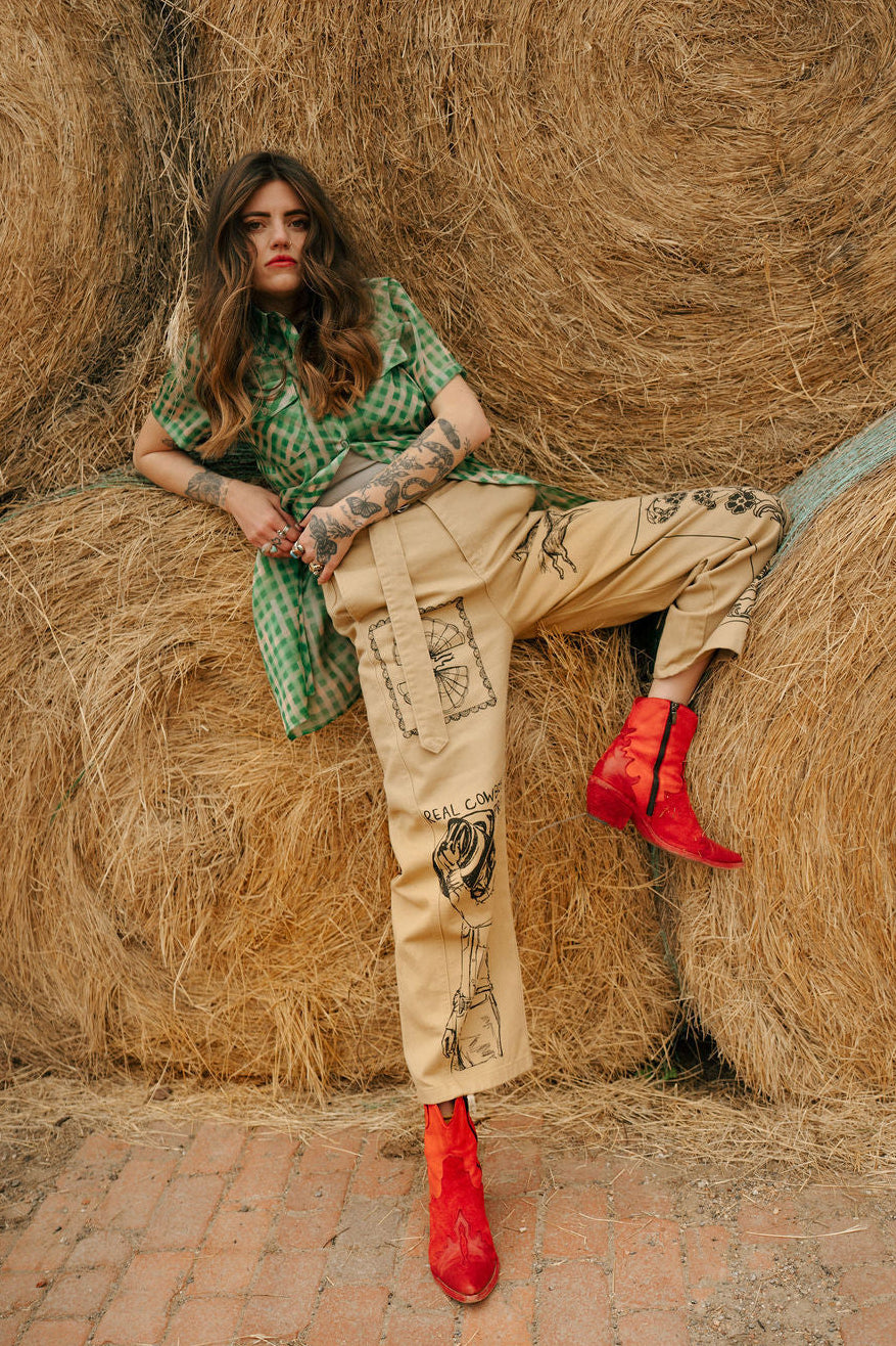Woman sitting on hay bales wearing a green top, beige pants, and red shoes.