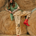 Woman sitting on hay bales wearing a green top, beige pants, and red shoes.