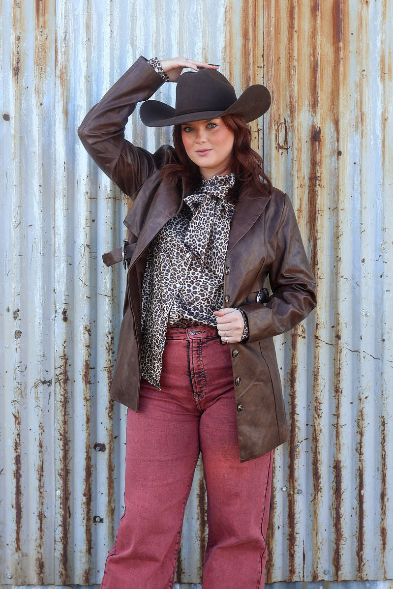 Person wearing a cowboy hat and brown leather jacket against a rusty corrugated metal wall