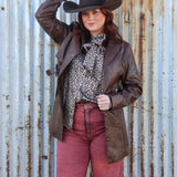Person wearing a cowboy hat and brown leather jacket against a rusty corrugated metal wall