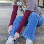 Person sitting on steps wearing a cowboy hat, jeans, and boots in front of a small building.